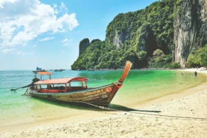 Traditionele longtailboot op een wit strand met groene kalksteenrotsen in Krabi, Thailand