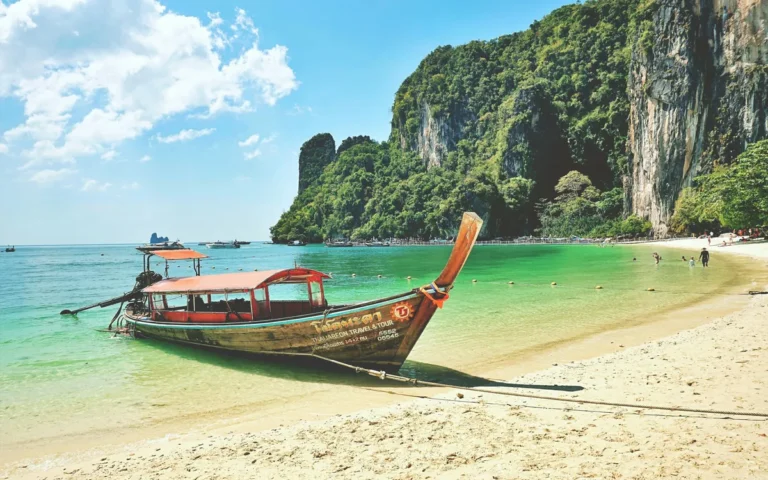 Traditionele longtailboot op een wit strand met groene kalksteenrotsen in Krabi, Thailand