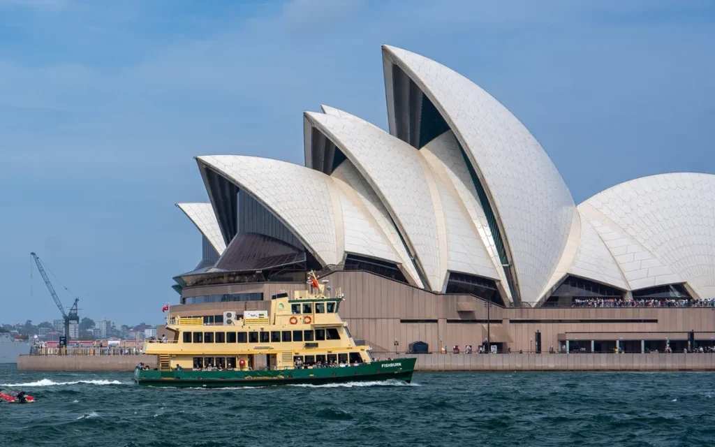 Het operagebouw van Sydney aan de haven met een groen-gele veerboot op het water