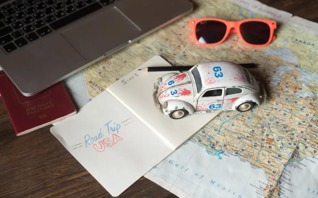 Paspoort, laptop, zonnebril en een speelgoedautootje op een kaart van de Verenigde Staten
