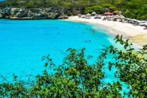 Baai met wit zandstrand, turquoise water en strandparasols tussen groene kliffen op Curaçao