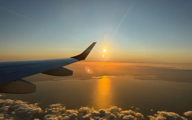 Uitzicht vanuit een vliegtuigraam op de vleugel met een laagstaande zon boven wolken en zee
