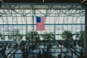 Vertrekhal van een Amerikaans vliegveld met een grote Amerikaanse vlag voor de glazen gevel en vliegtuigen buiten